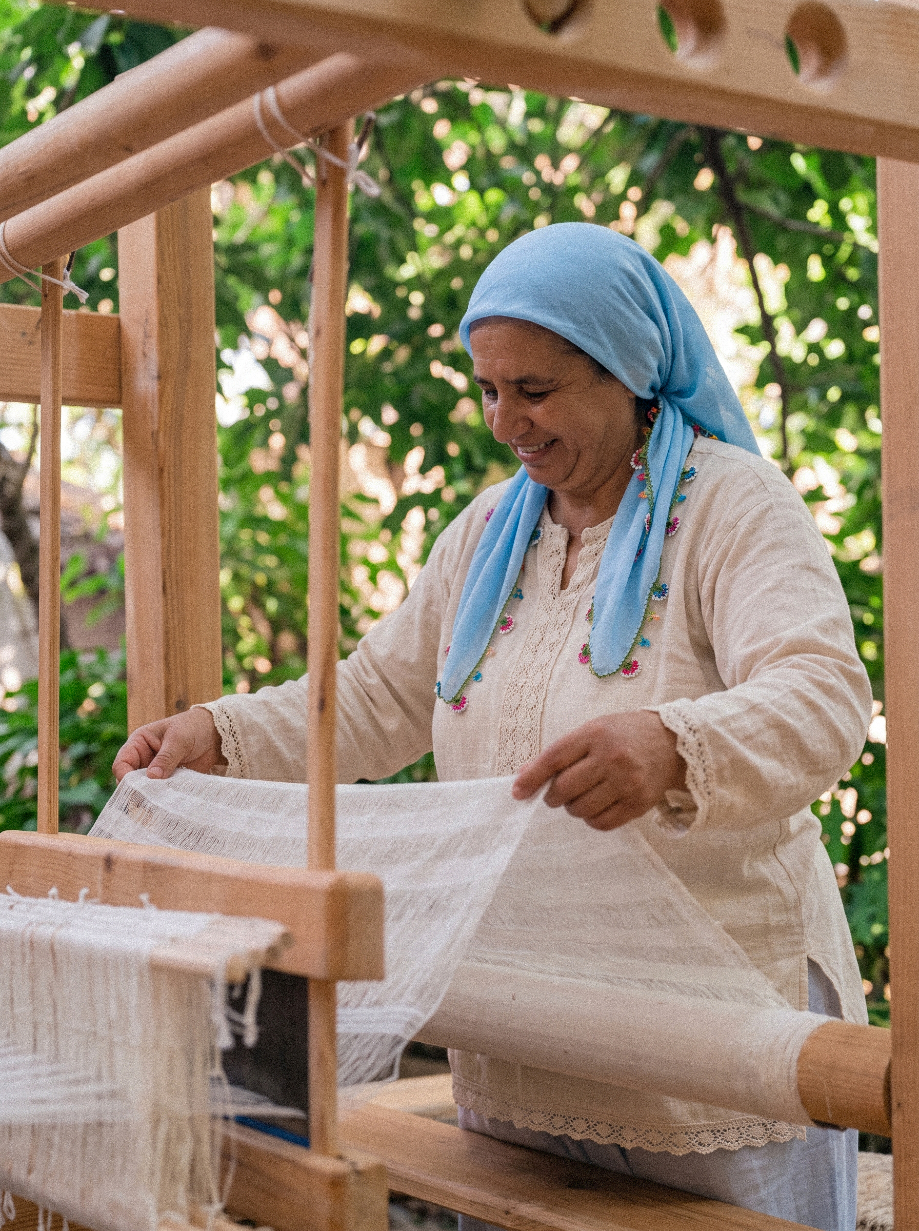 A weaver at a traditional loom, skeins of coloured wool hanging above