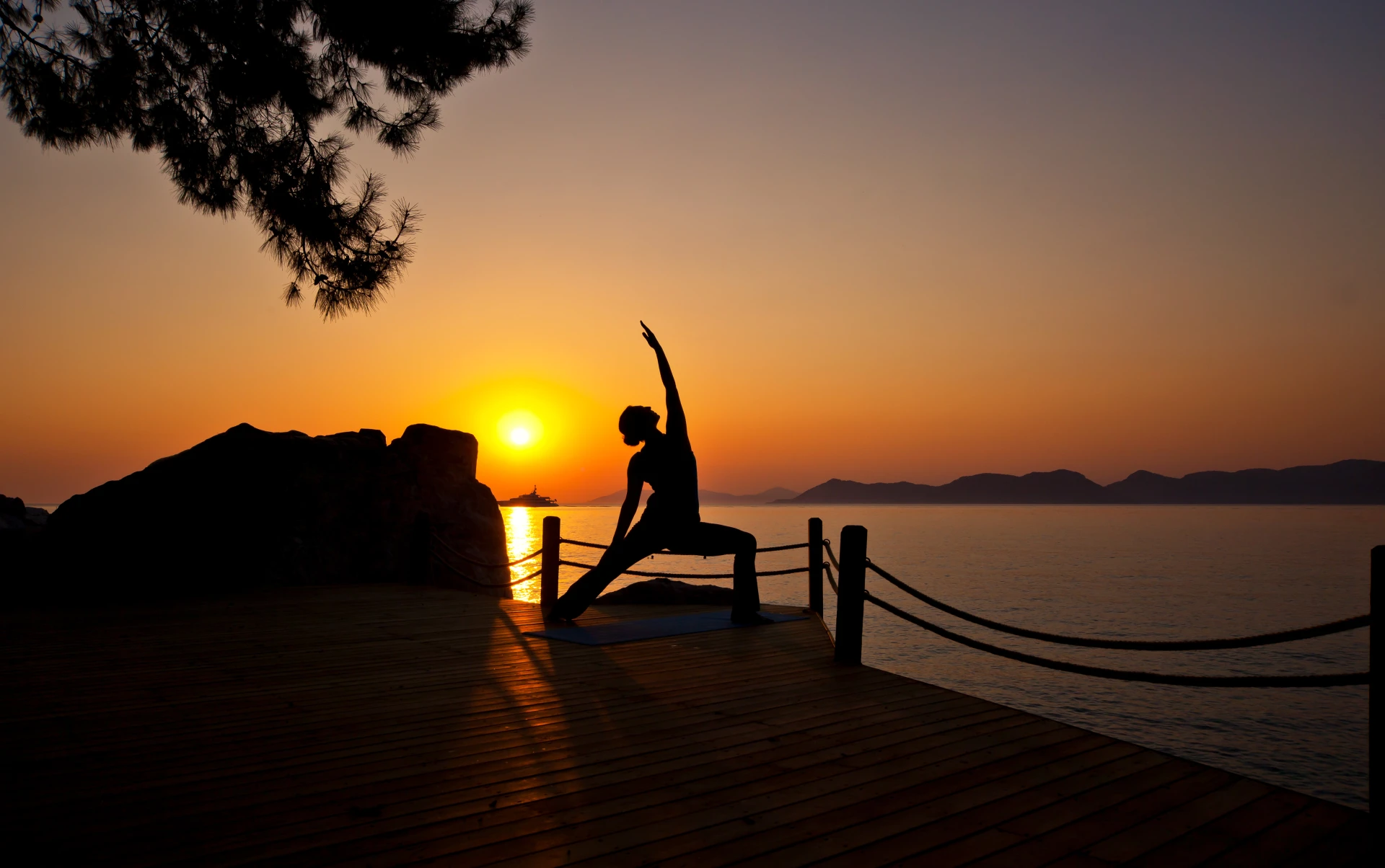 A yoga session on a seaside deck as the sun sets behind the hills
